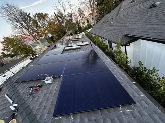 Solar modules being set on a shingle roof at dusk, with skylights and trees beyond, Studio City