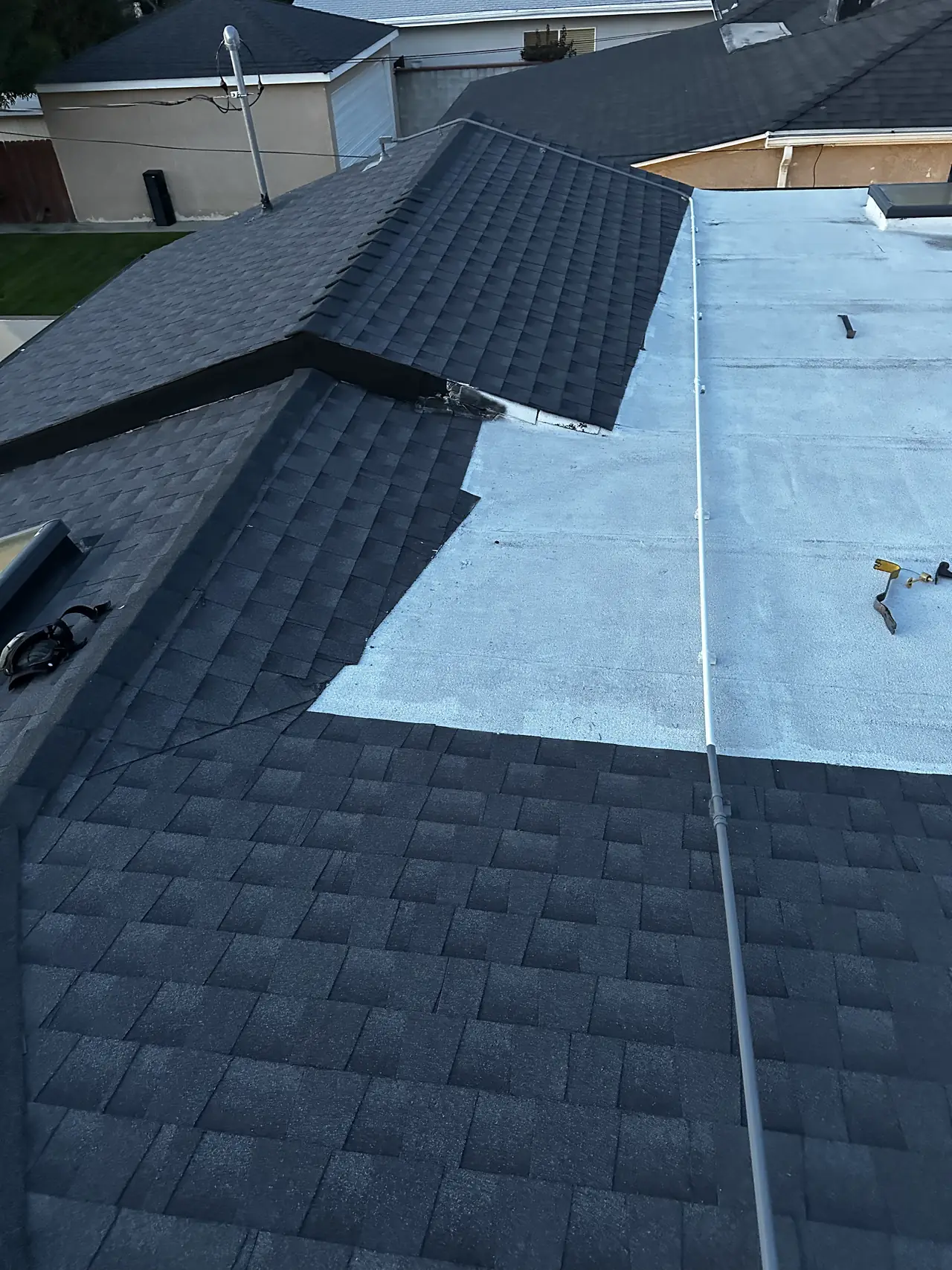 A shingle roof slope meeting a light-colored low-slope roof section on the same house, with a conduit run across it, Studio City