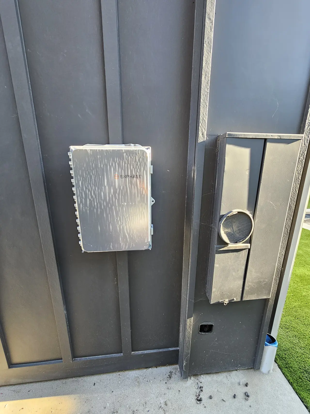An electrical combiner enclosure mounted on a dark board-and-batten wall beside an empty meter socket ring, Studio City