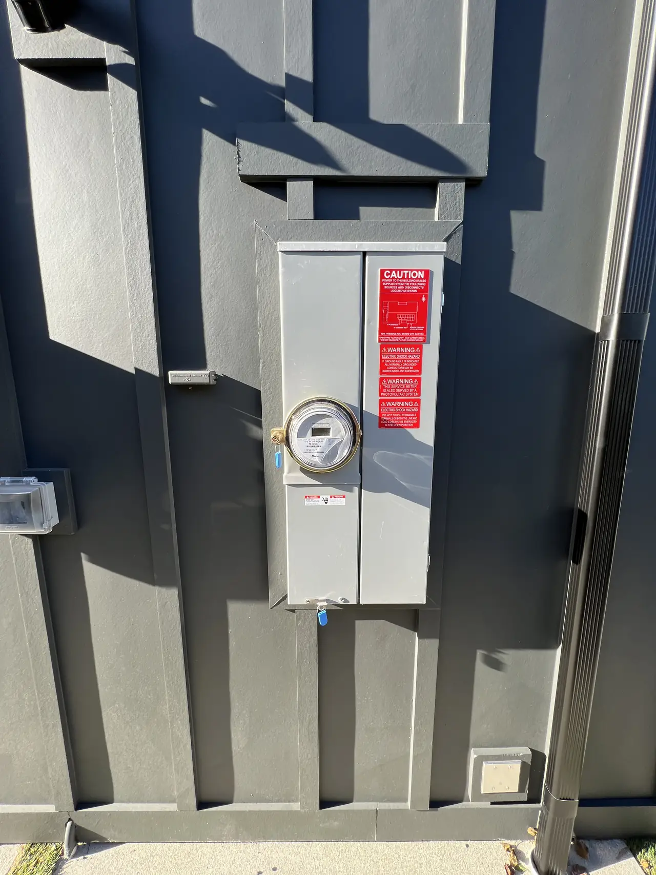A combination meter and main breaker enclosure mounted on a dark board-and-batten wall with red warning placards, Studio City