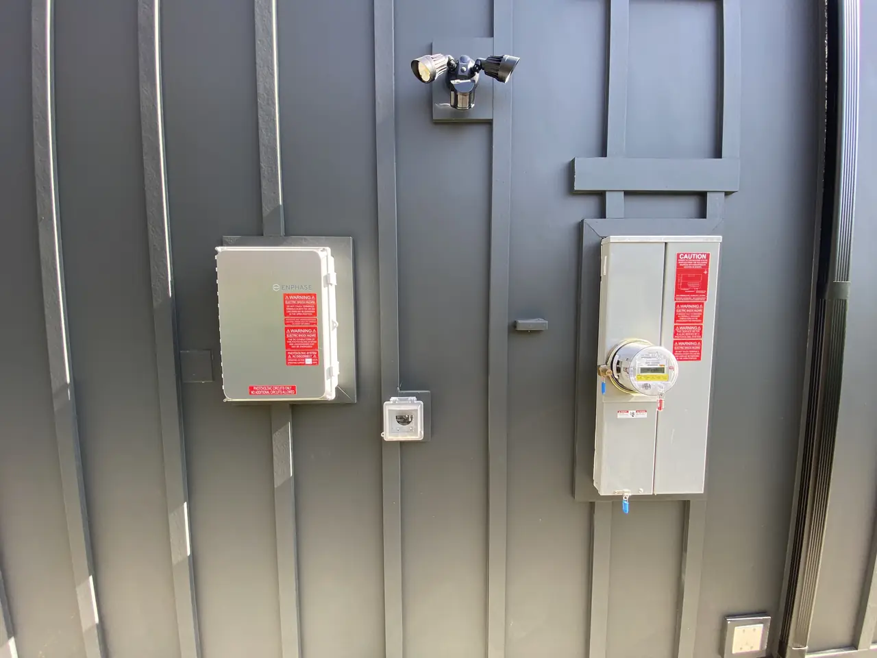 Two closed electrical enclosures and a meter on a gray battened wall beneath a floodlight, Studio City