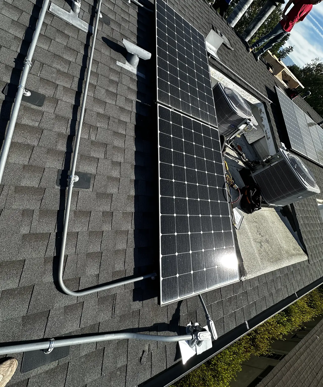 A solar module lifted off its rails and standing on edge on a shingle roof beside the racking and re-routed conduit, Studio City