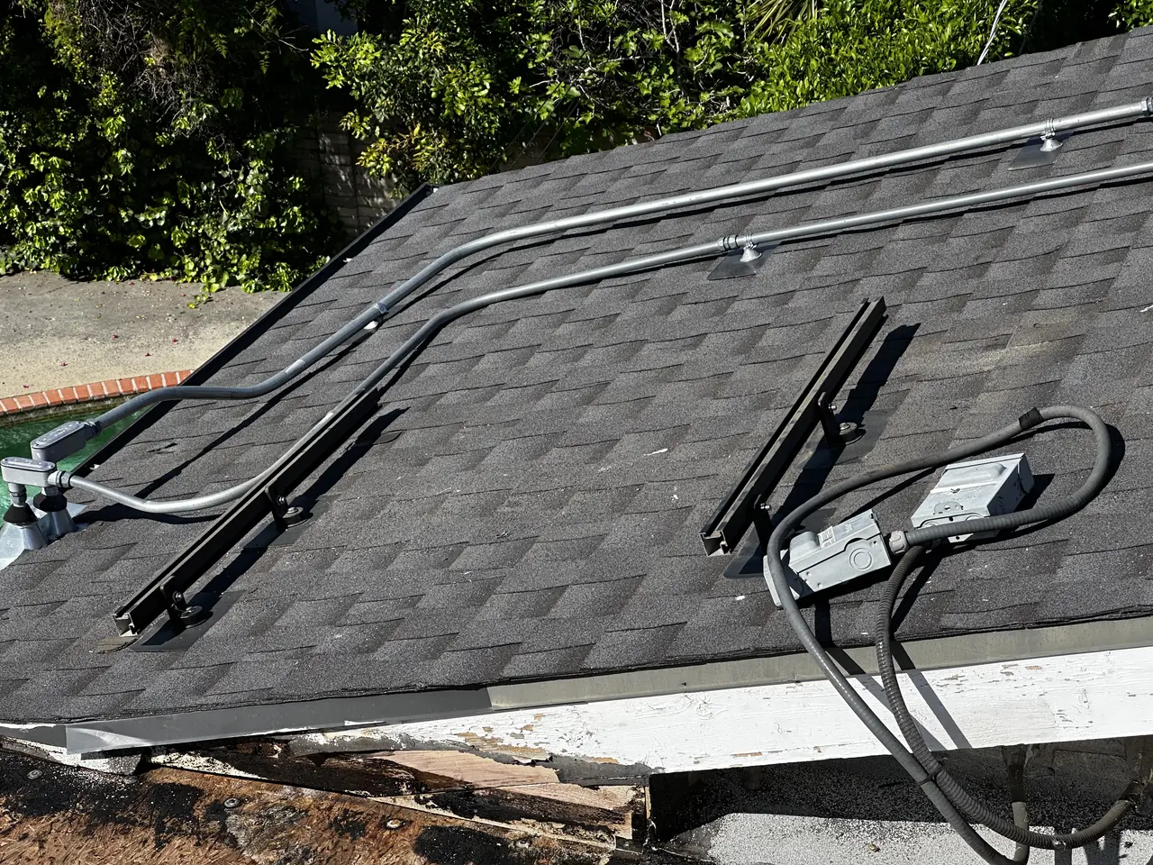 Mounting rails and conduit on a shingle roof beside a section where the covering has been opened at the edge, Studio City