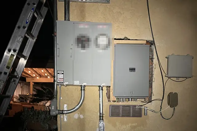 A new two-meter electrical service and a panel set into a stucco wall, lit by a work light, Sunland