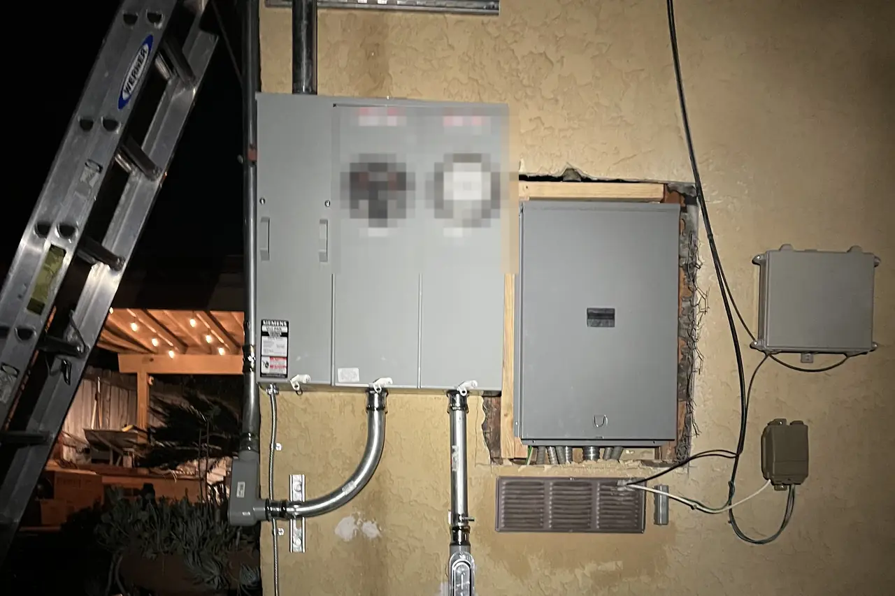 A new two-meter electrical service and a panel set into a stucco wall, lit by a work light, Sunland