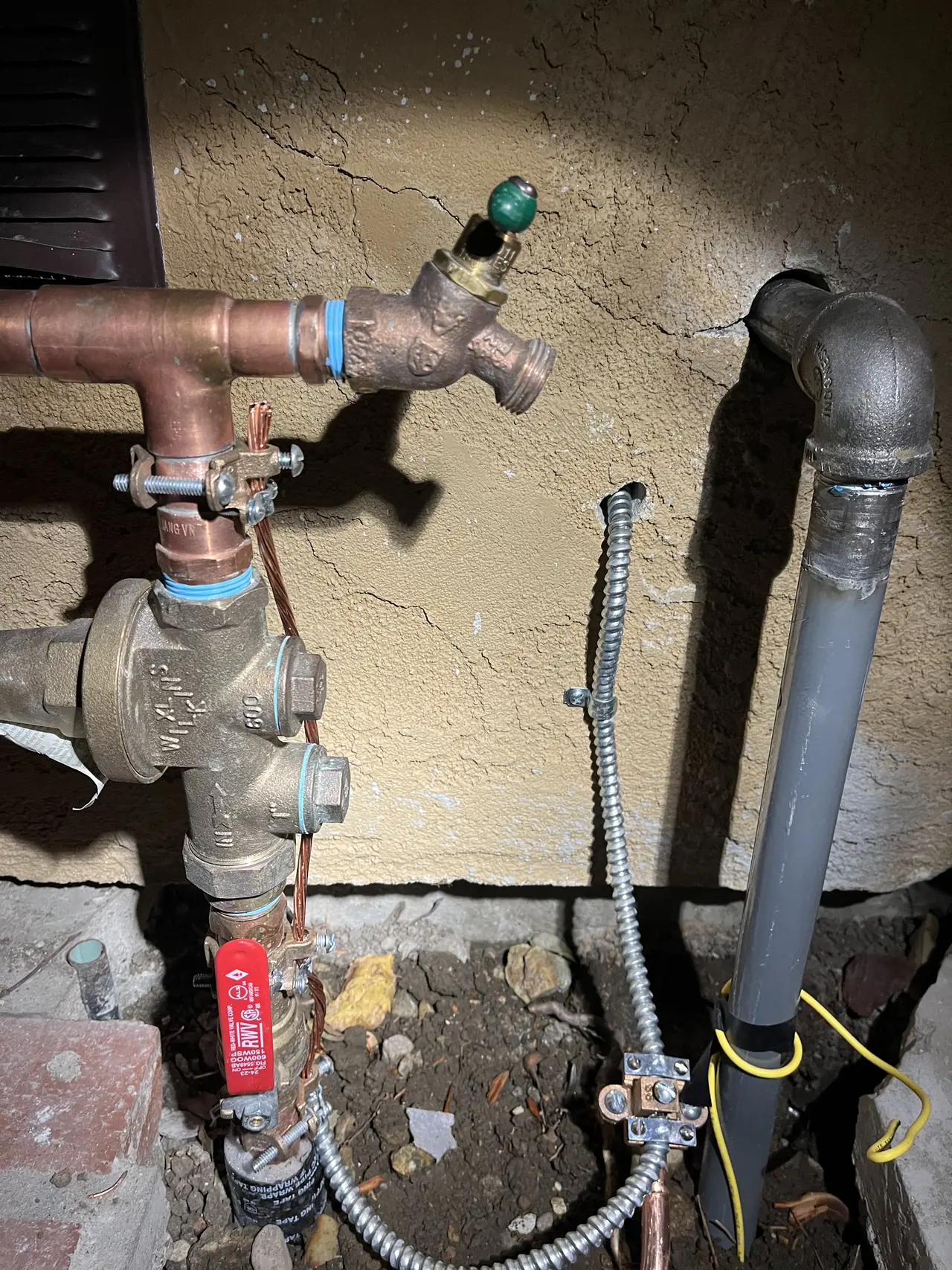 A bare copper bonding conductor clamped to copper water piping beside a gas line at the base of a stucco wall, Sunland