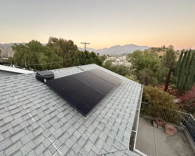 Black solar modules on a gray shingle roof at sunset with foothills behind, Sunland