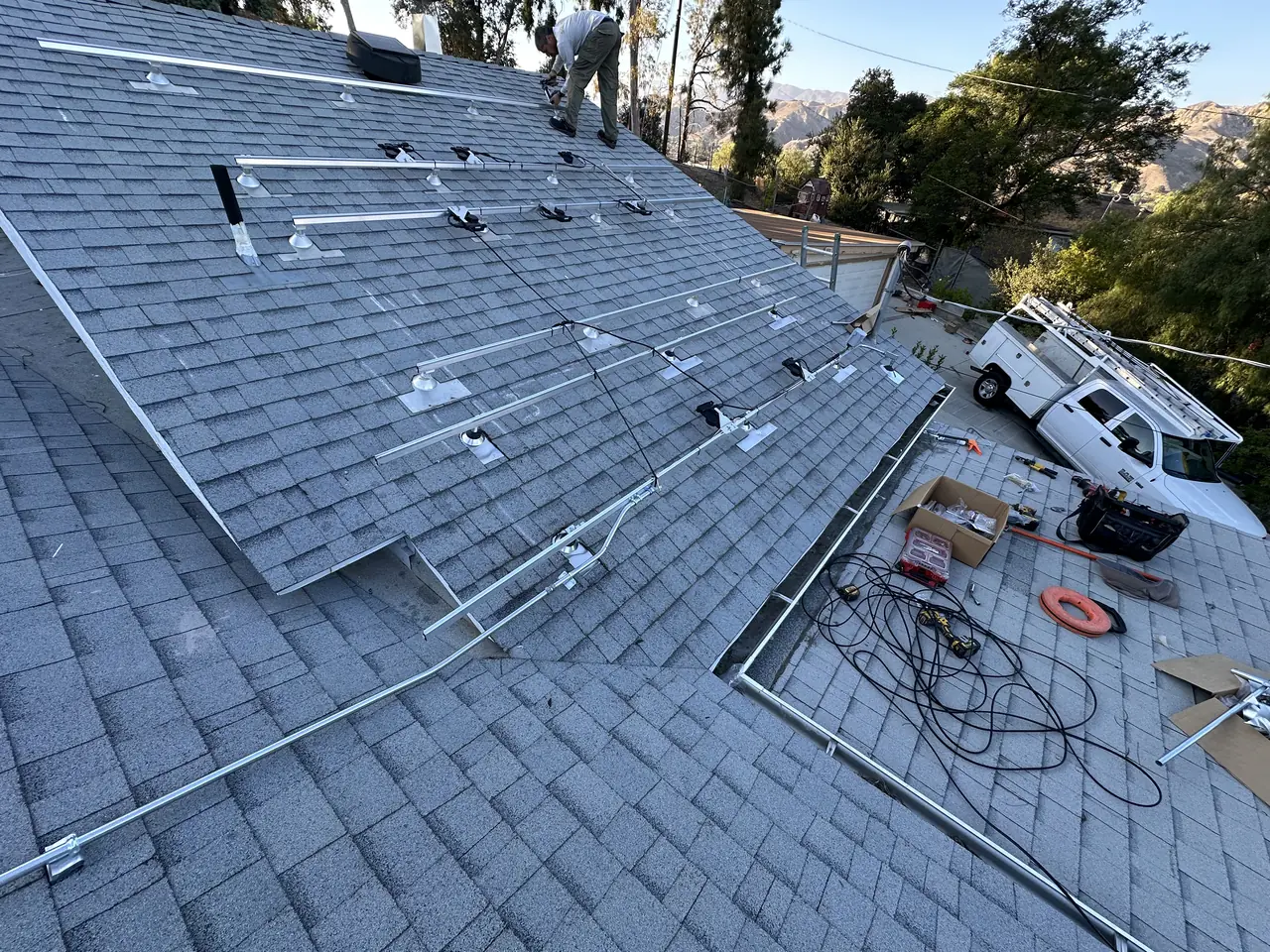 Aluminum rails with Enphase microinverters on a shingle roof before the modules, a work truck below, Sunland