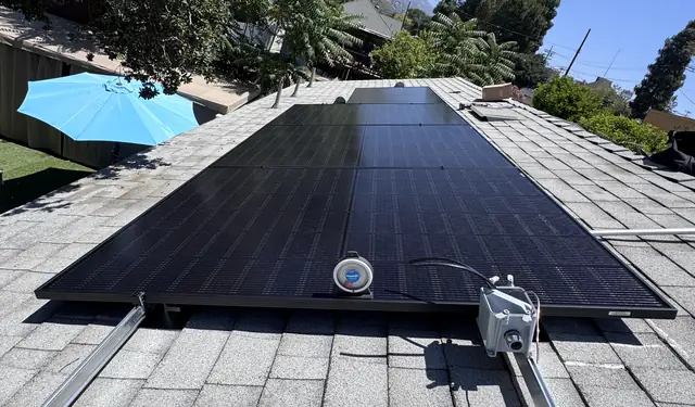 Black solar modules on a gray shingle roof with an inclinometer on the array and a junction box on the rail, Sunland