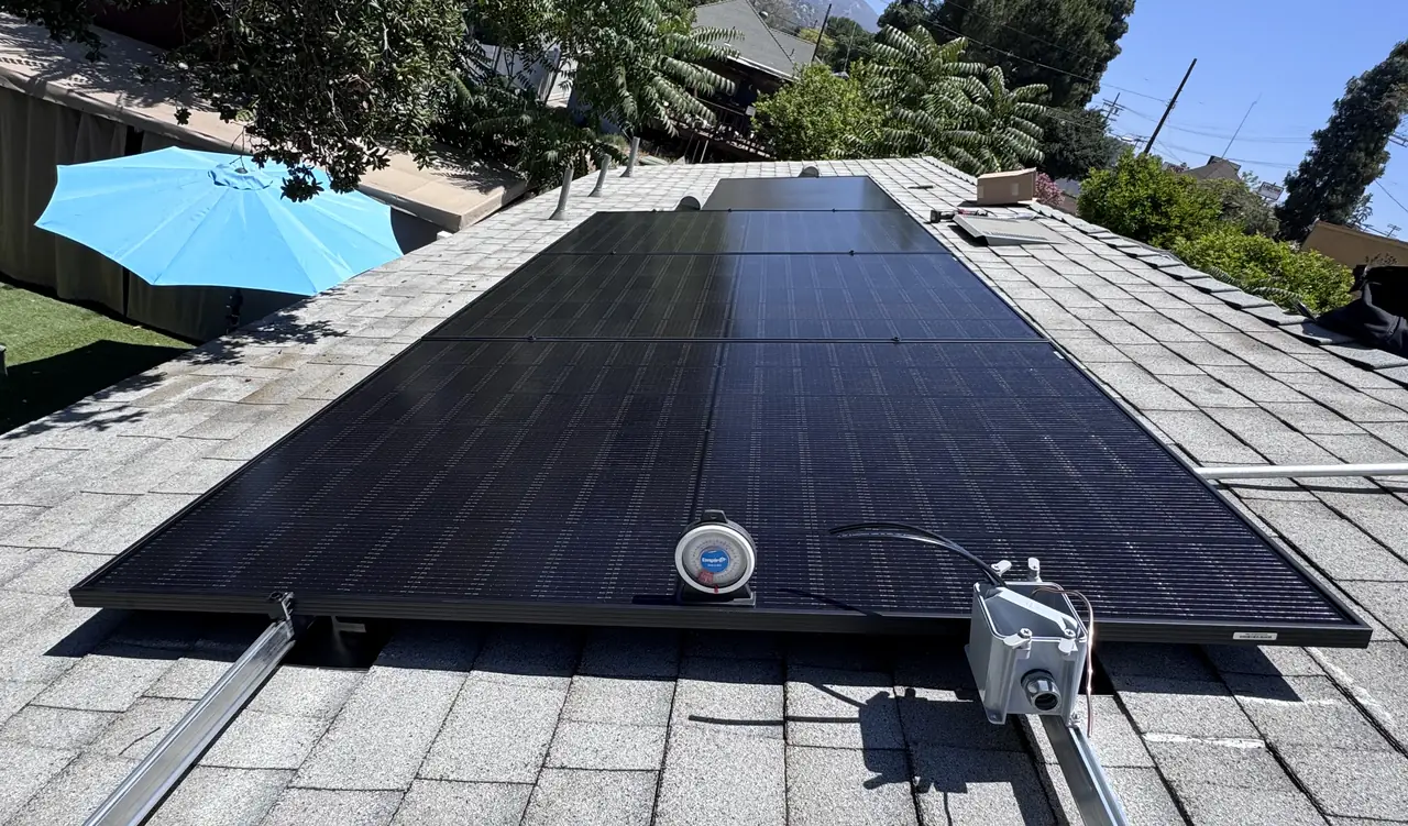 Black solar modules on a gray shingle roof with an inclinometer on the array and a junction box on the rail, Sunland