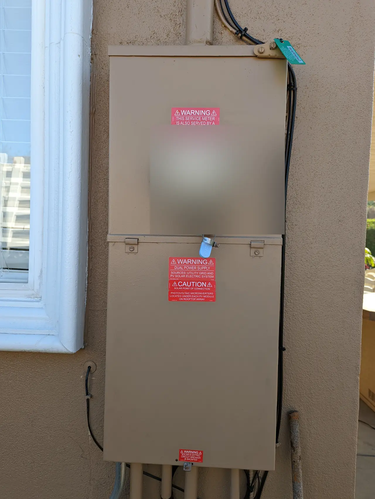 Meter panel with solar warning labels on a stucco wall, the meter face obscured, Tarzana