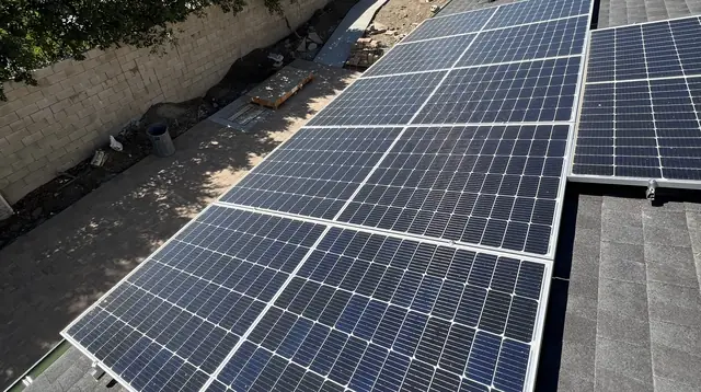 Seven solar modules on the composition shingle roof of a new detached ADU, with the block wall and the rear yard beside it, Tarzana