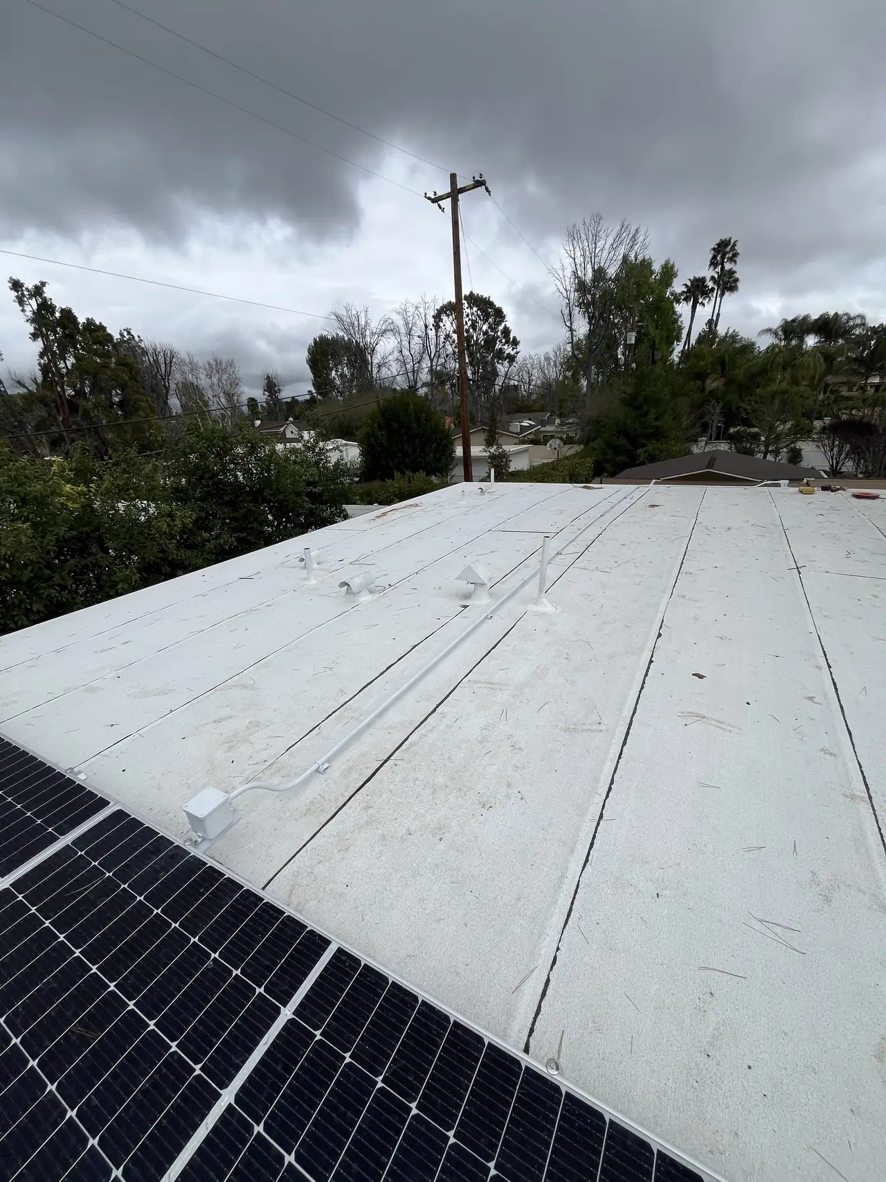 Solar modules along the edge of a low-slope white membrane roof under an overcast sky, Tarzana