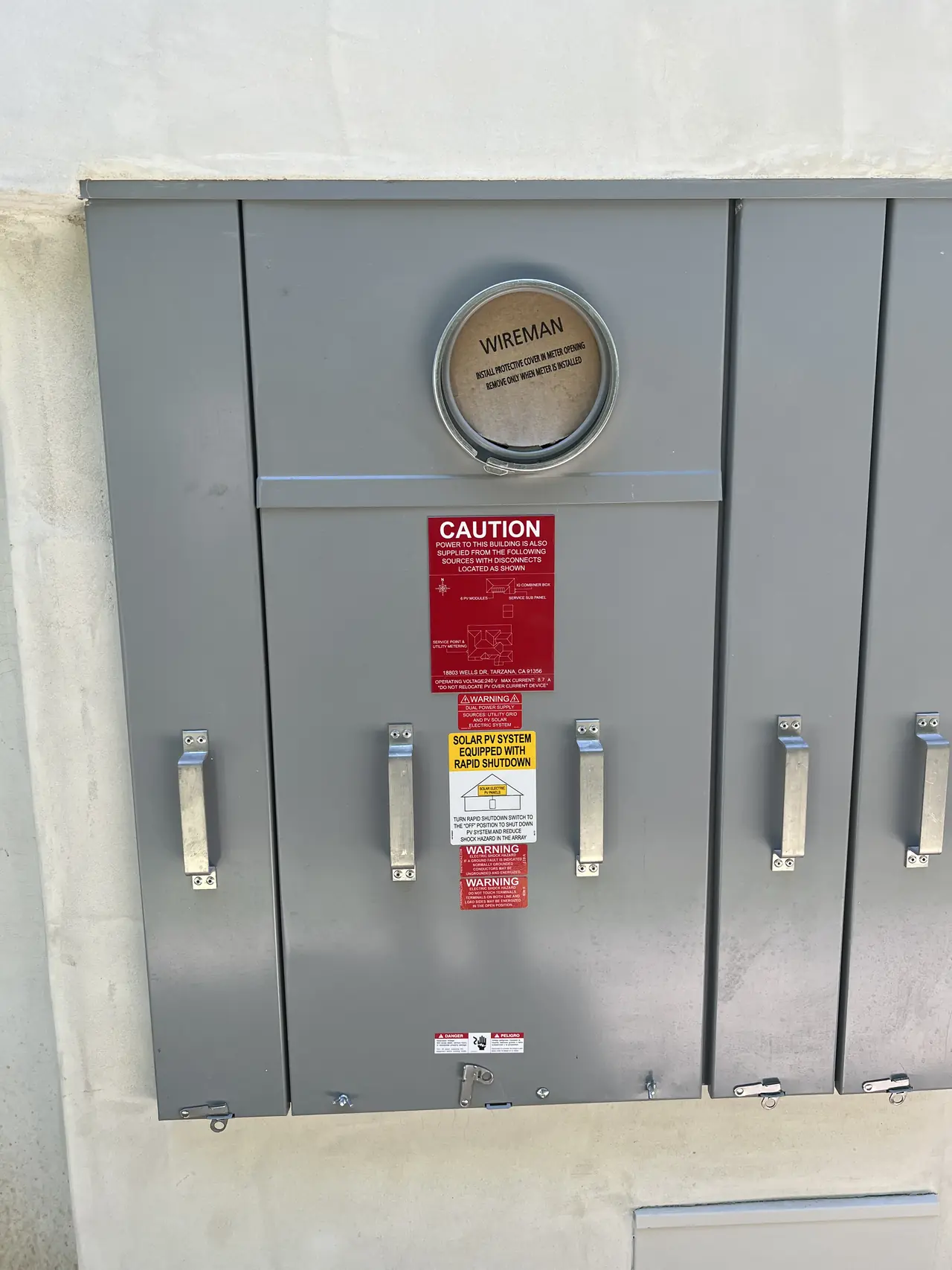 Gray main service panel on a new stucco wall with solar warning and rapid shutdown labels, Tarzana