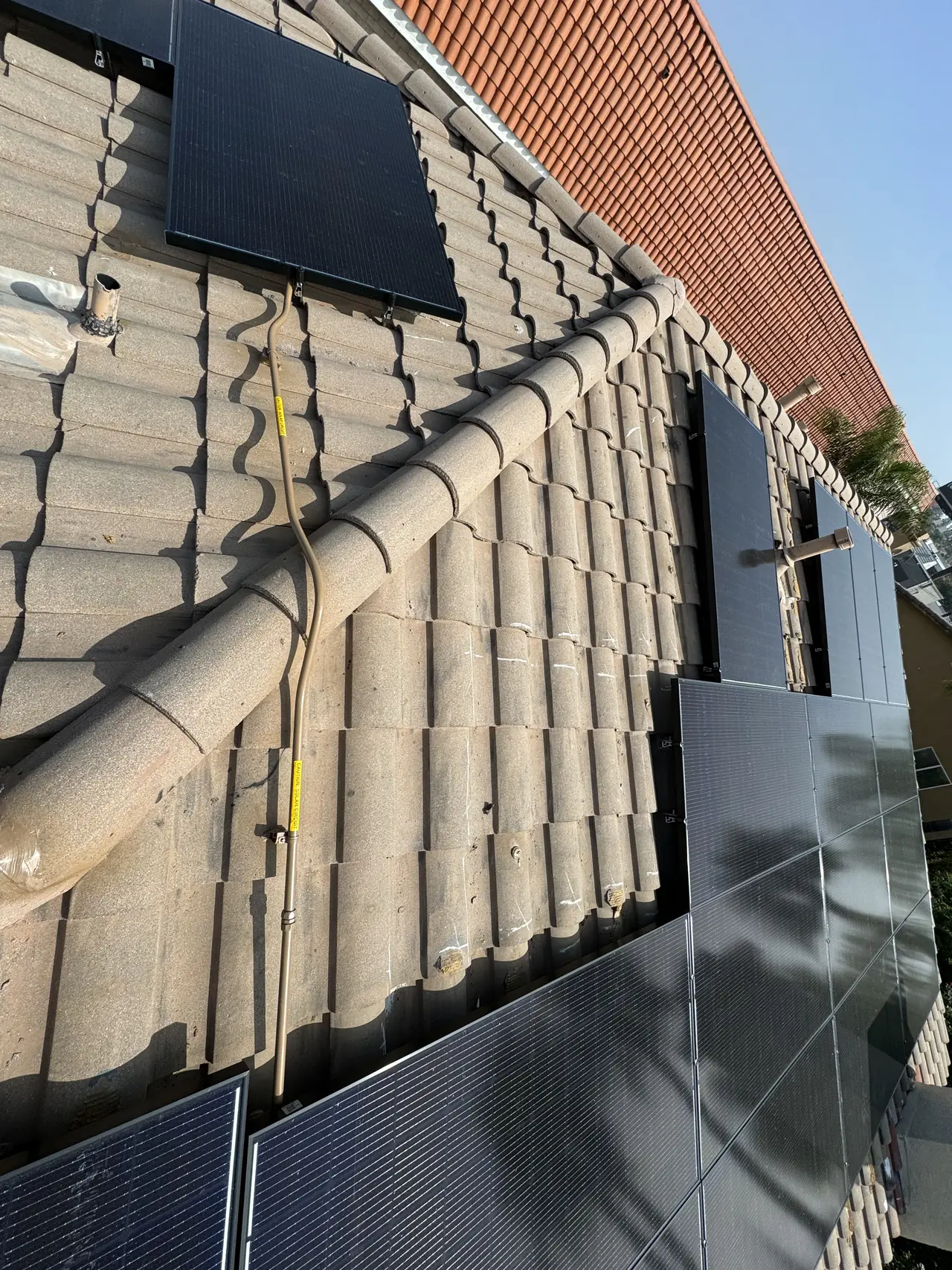 Solar modules on a concrete S-tile roof plane meeting the eave, with the conduit run along the tile, Tarzana
