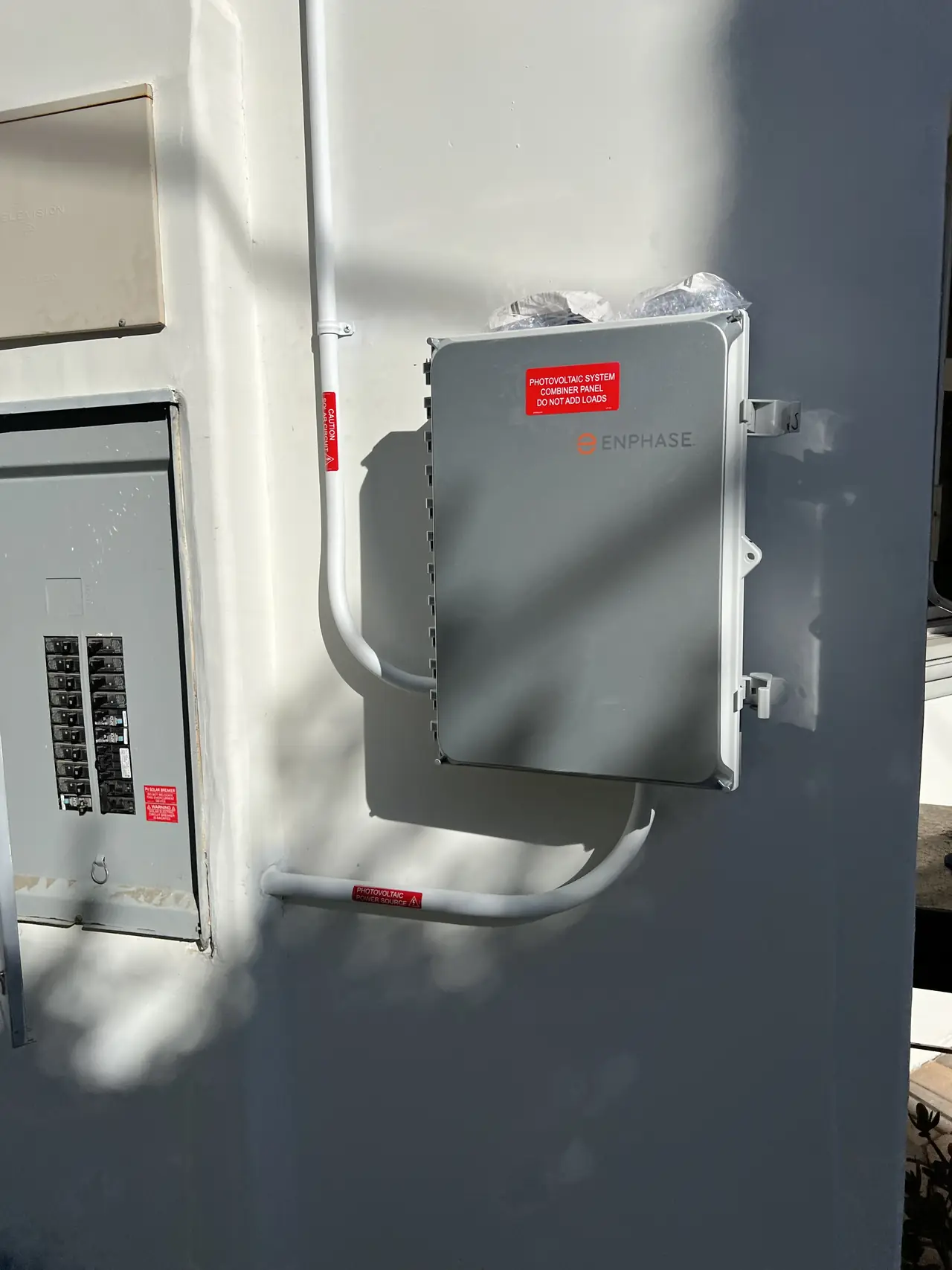 Enphase combiner mounted on a stucco wall beside the service panel, with conduit from above and a solar circuit label, Tarzana