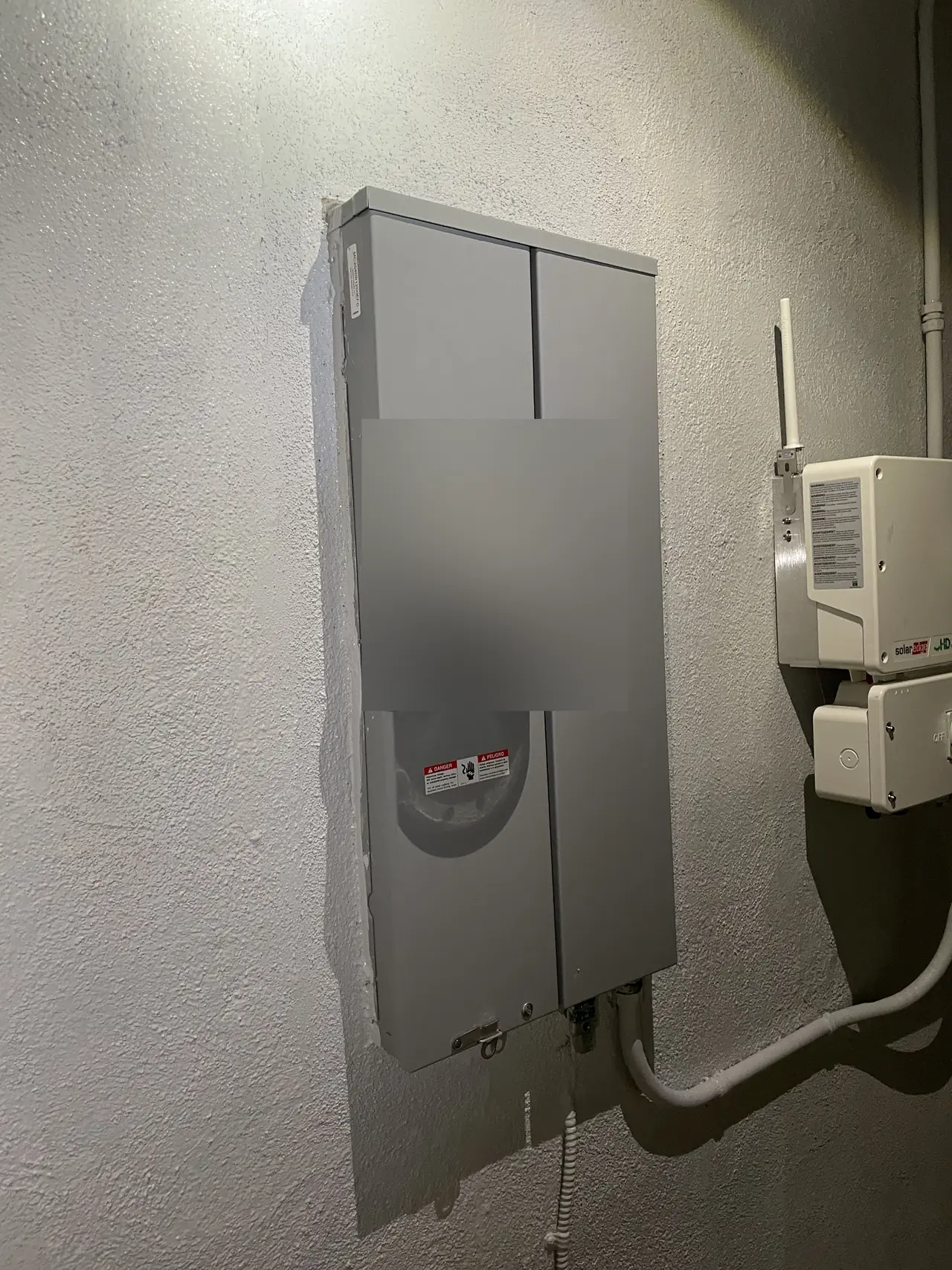 New gray meter panel set into patched stucco on a side wall, the meter face obscured, with the inverter beside it, Tarzana