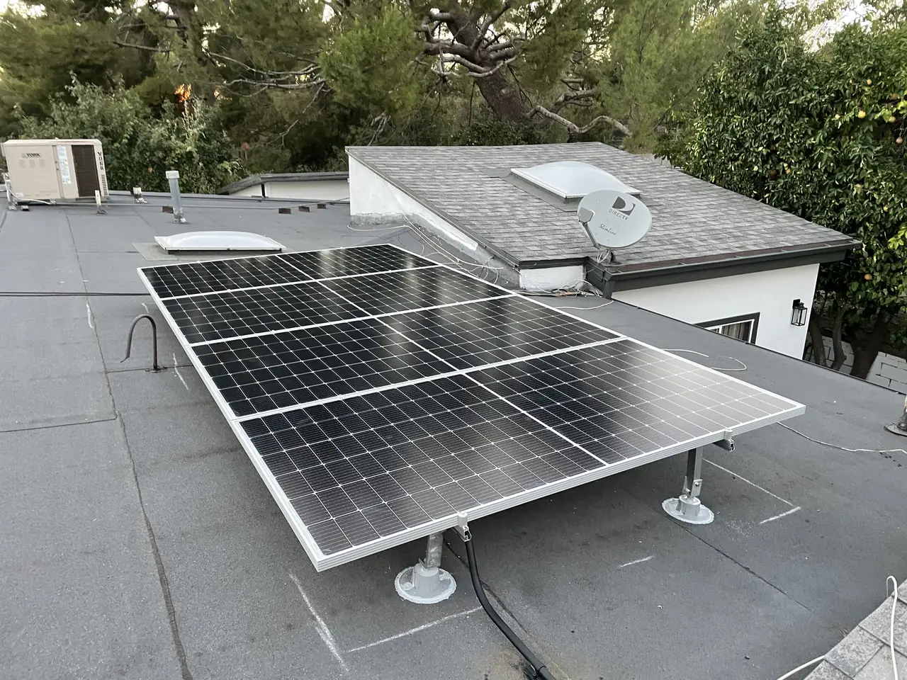 A second group of solar modules on tilt legs over a low-slope roof, with skylights and a satellite dish, Tujunga