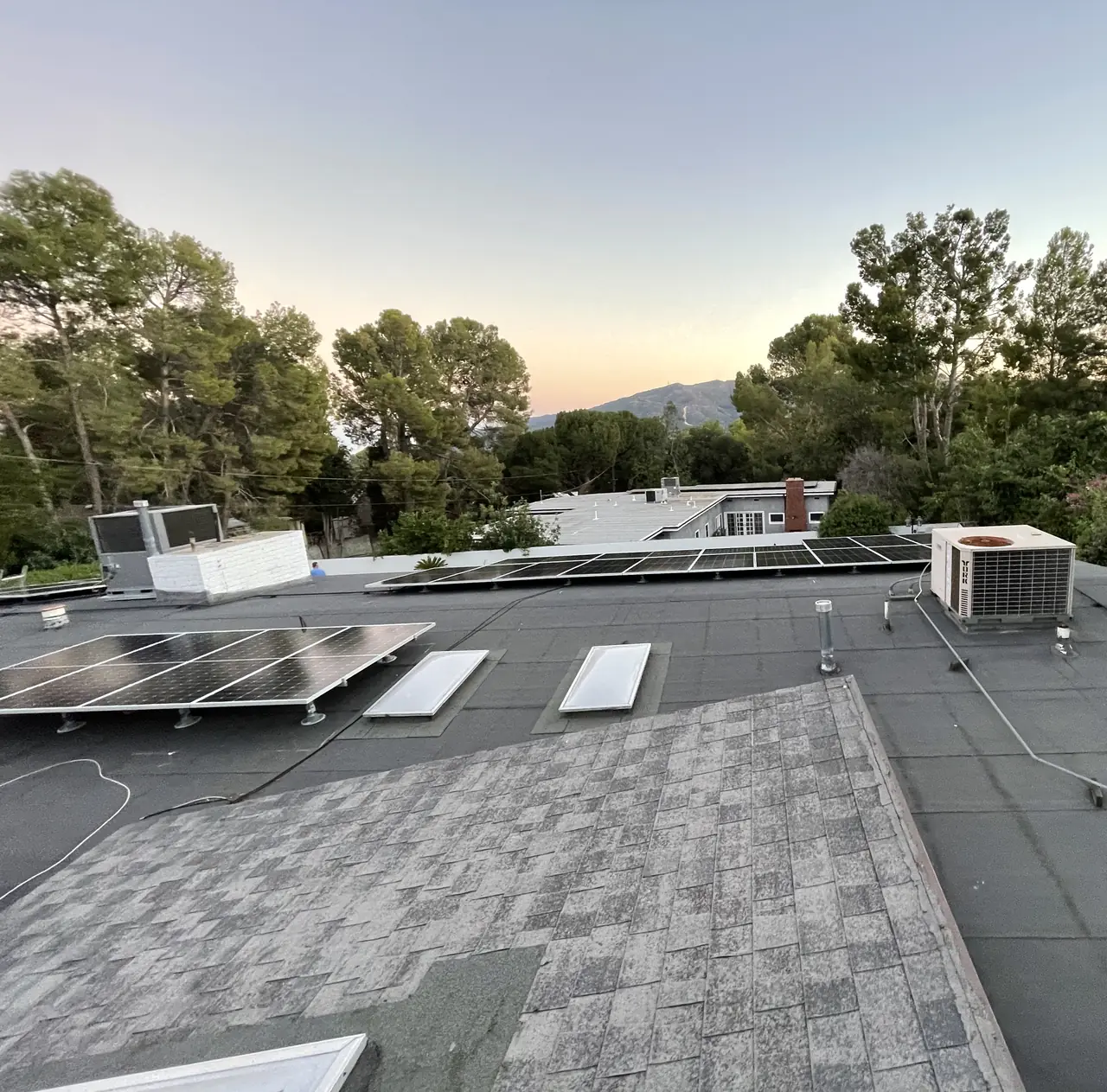 A low-slope roof with solar modules and a pitched shingle section, with foothills on the horizon, Tujunga