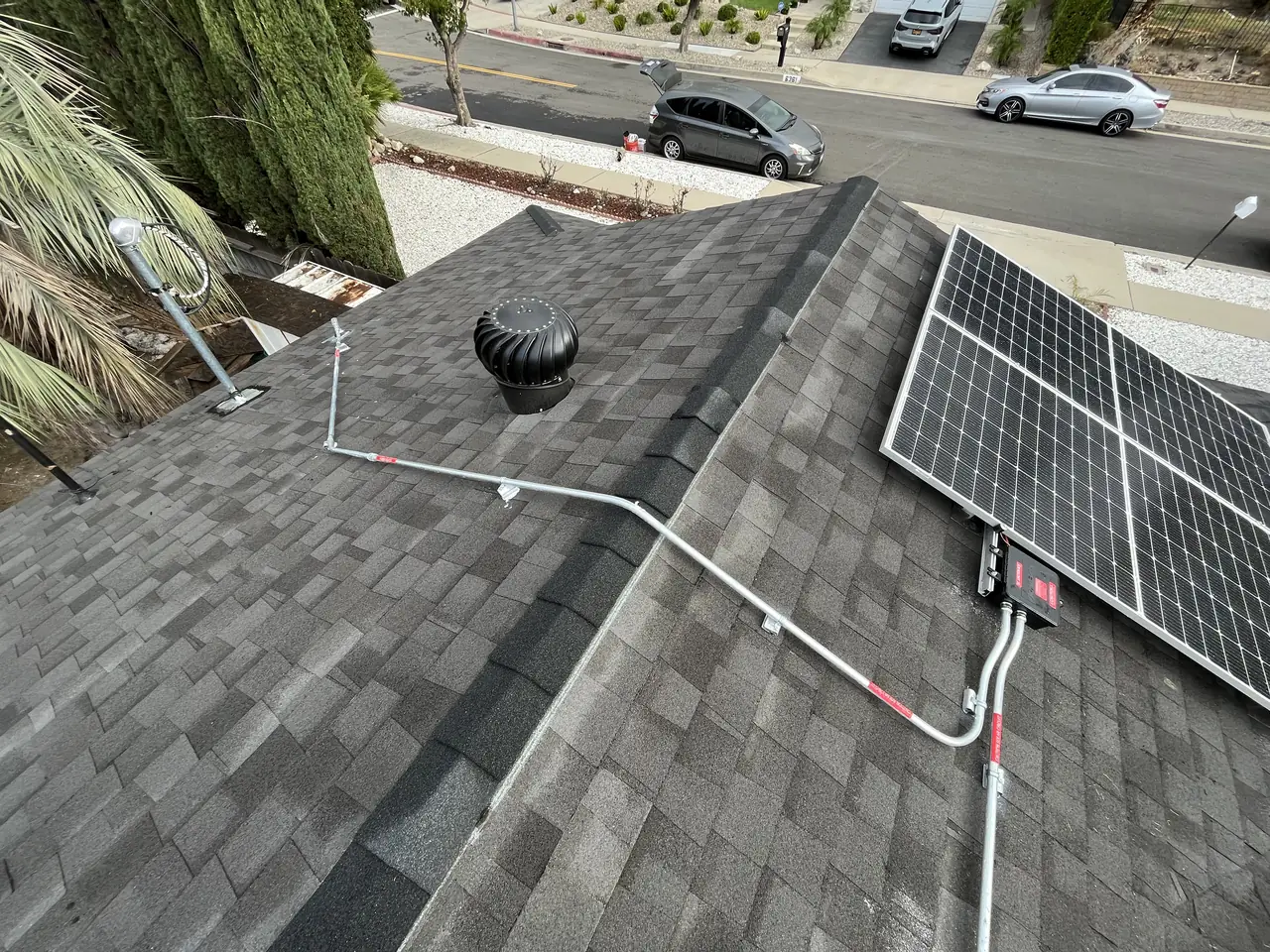 Conduit running over a shingle roof ridge from a solar array, a turbine vent and the street below, Tujunga