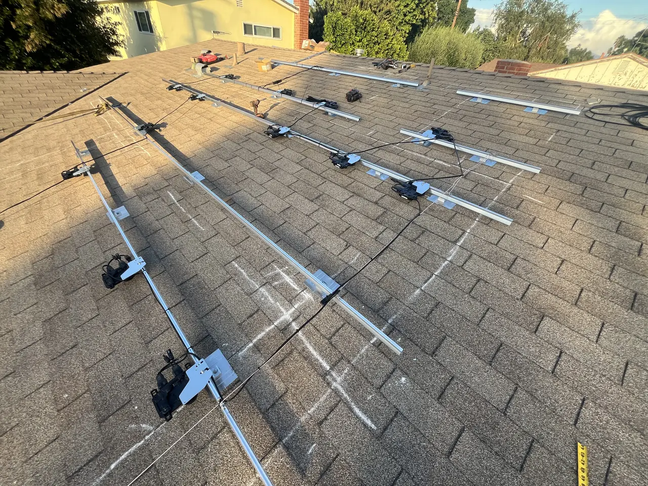 Aluminum mounting rails laid out across a shingle roof before the modules go on, with a suburban street beyond, Van Nuys, Los Angeles
