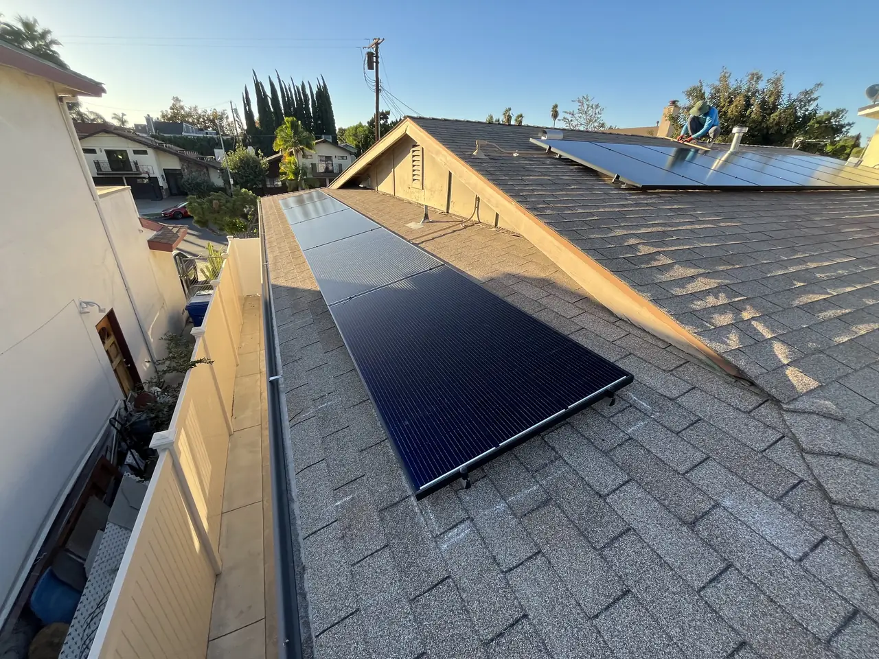 Black modules on the far slope of a shingle roof with rooftops and trees in the background, Van Nuys, Los Angeles