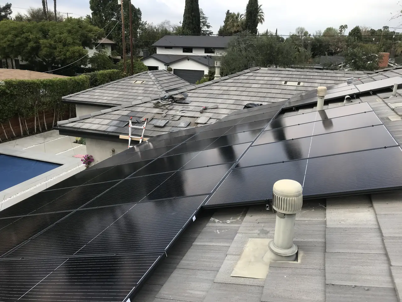 Black modules near the edge of a tile roof with a pool deck and hedge below, Van Nuys, Los Angeles