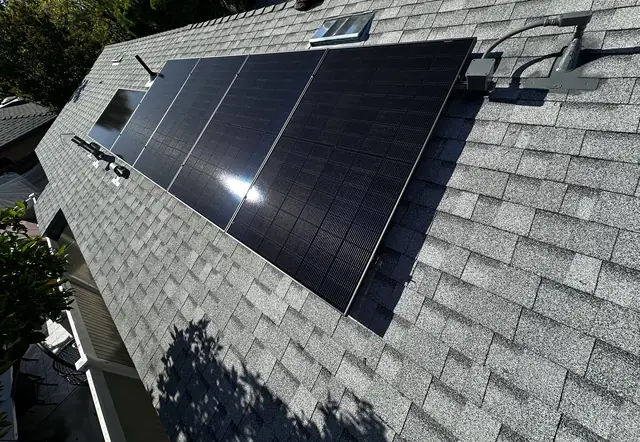 A small array of black modules with sun glint on the slope of a new light-colored shingle roof, Van Nuys, Los Angeles