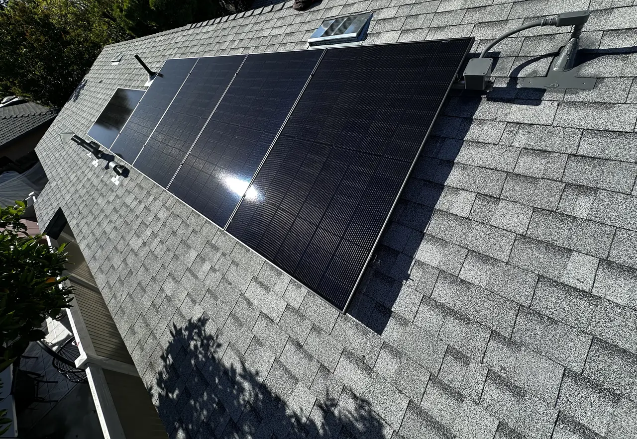 A small array of black modules with sun glint on the slope of a new light-colored shingle roof, Van Nuys, Los Angeles