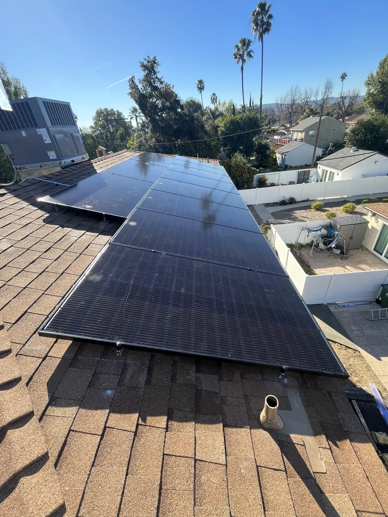 Black modules along the slope of a brown composition shingle roof with trees and a swimming pool beyond, Van Nuys, Los Angeles