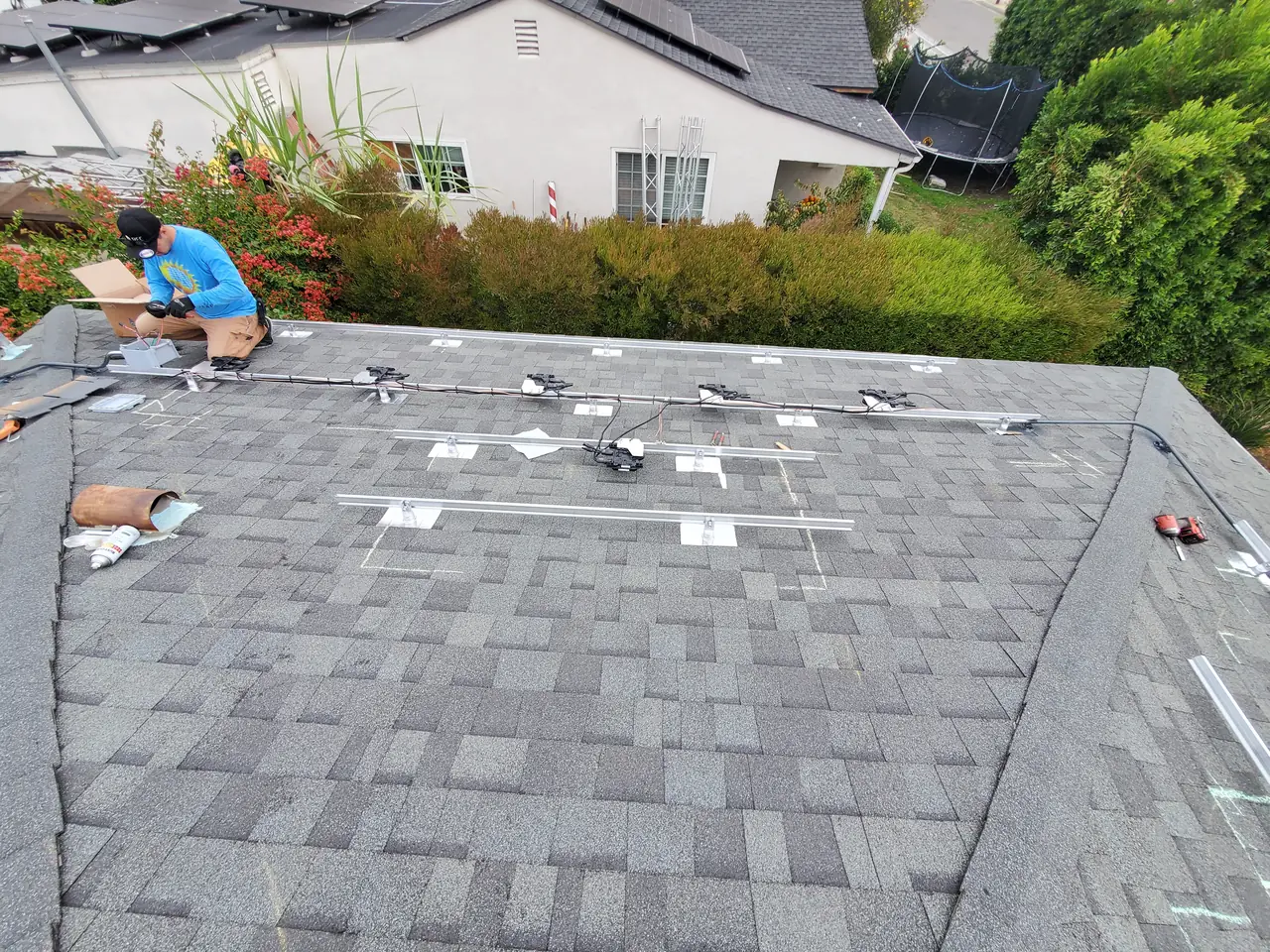 Mounting rails and flashing laid out across a dark shingle hip roof before the modules are installed, Van Nuys, Los Angeles