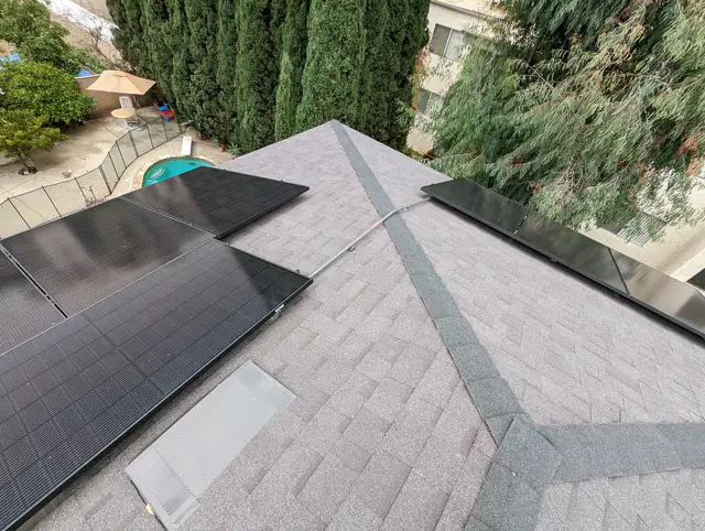 Black solar modules on the hip roof of a small building with a pool and garden below, Van Nuys, Los Angeles