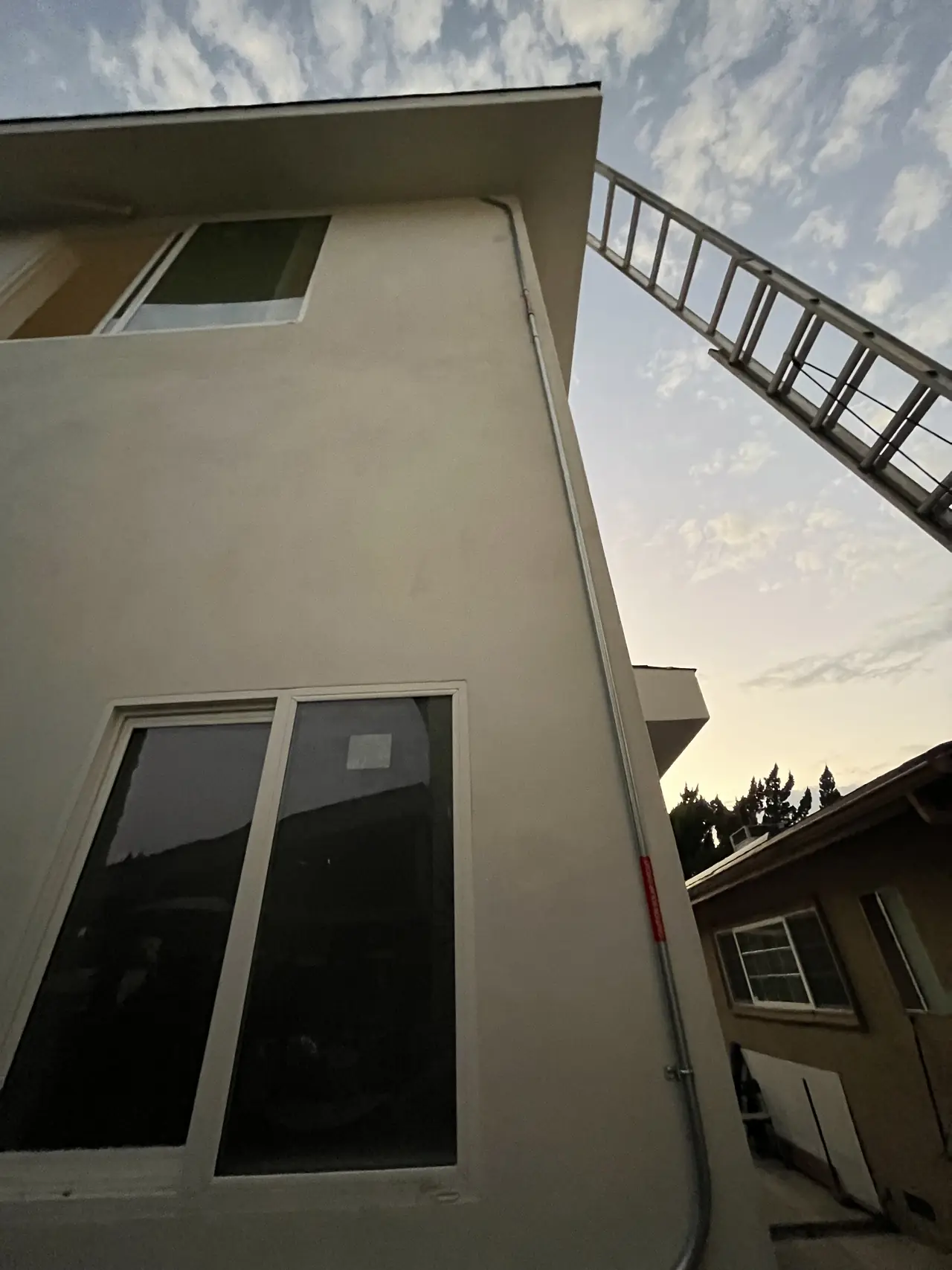The upper story of a new stucco building with a ladder against the wall and a clear sky above, Van Nuys, Los Angeles