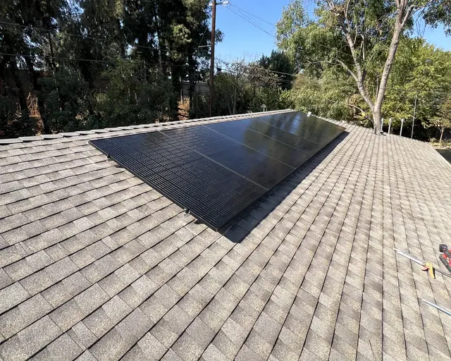 A small group of black modules near the ridge of a gray shingle hip roof under a clear blue sky, Van Nuys, Los Angeles