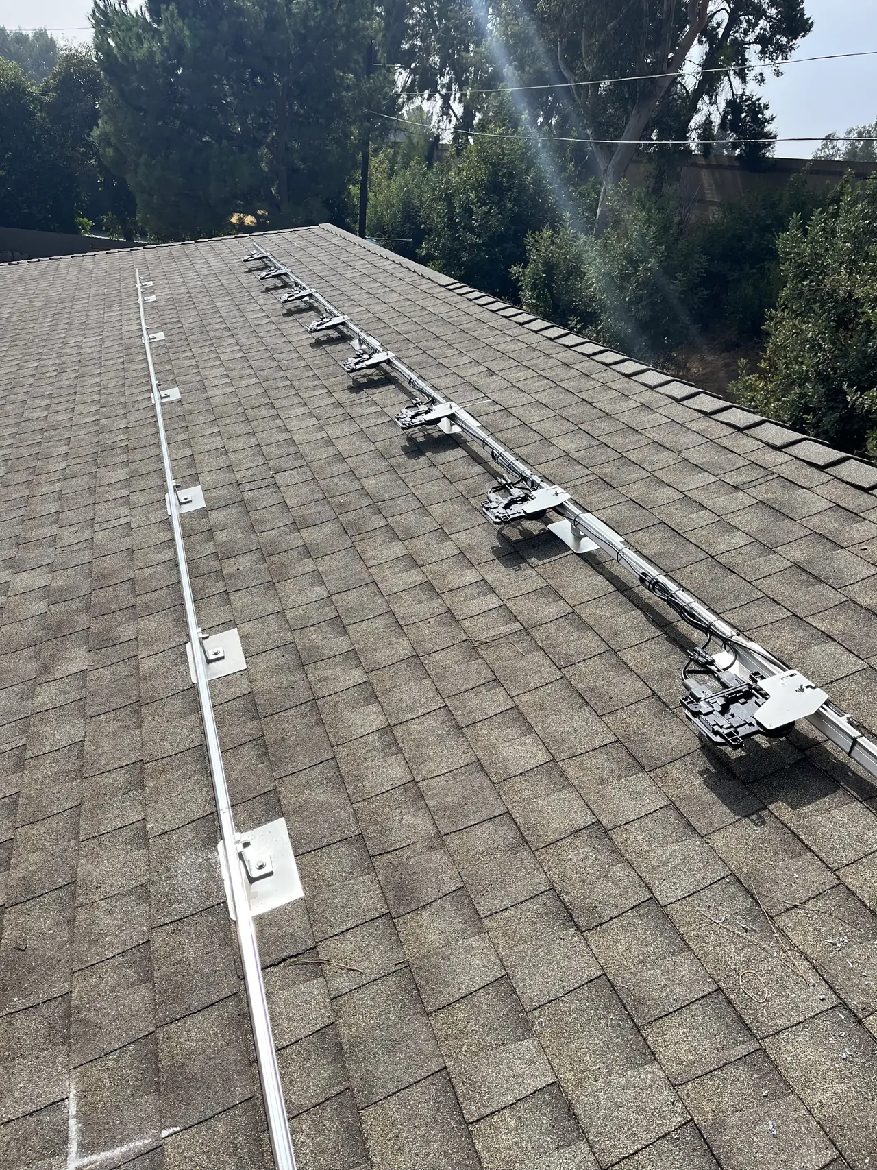 Mounting rails running across a gray shingle roof with a suburban street and trees behind, Van Nuys, Los Angeles
