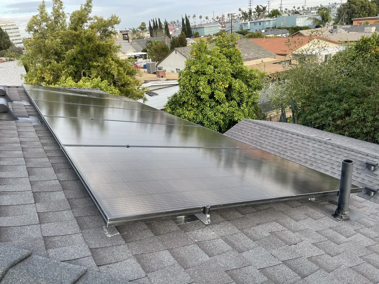 Black modules installed on the hip plane of a shingle roof with a clear sky above, Van Nuys, Los Angeles