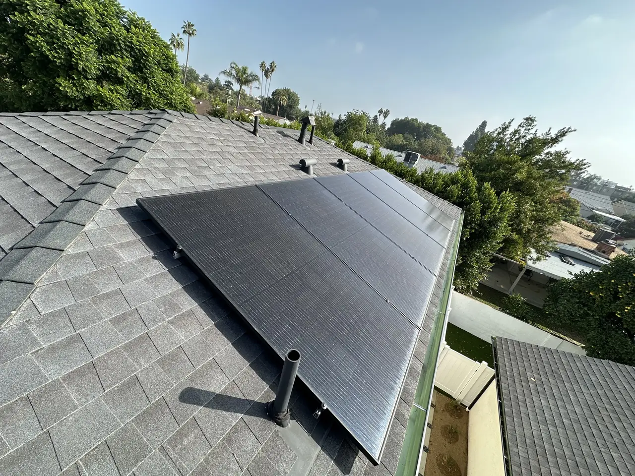 Wide view over the hip roof of a new dwelling with the array on one plane and neighboring roofs behind, Van Nuys, Los Angeles