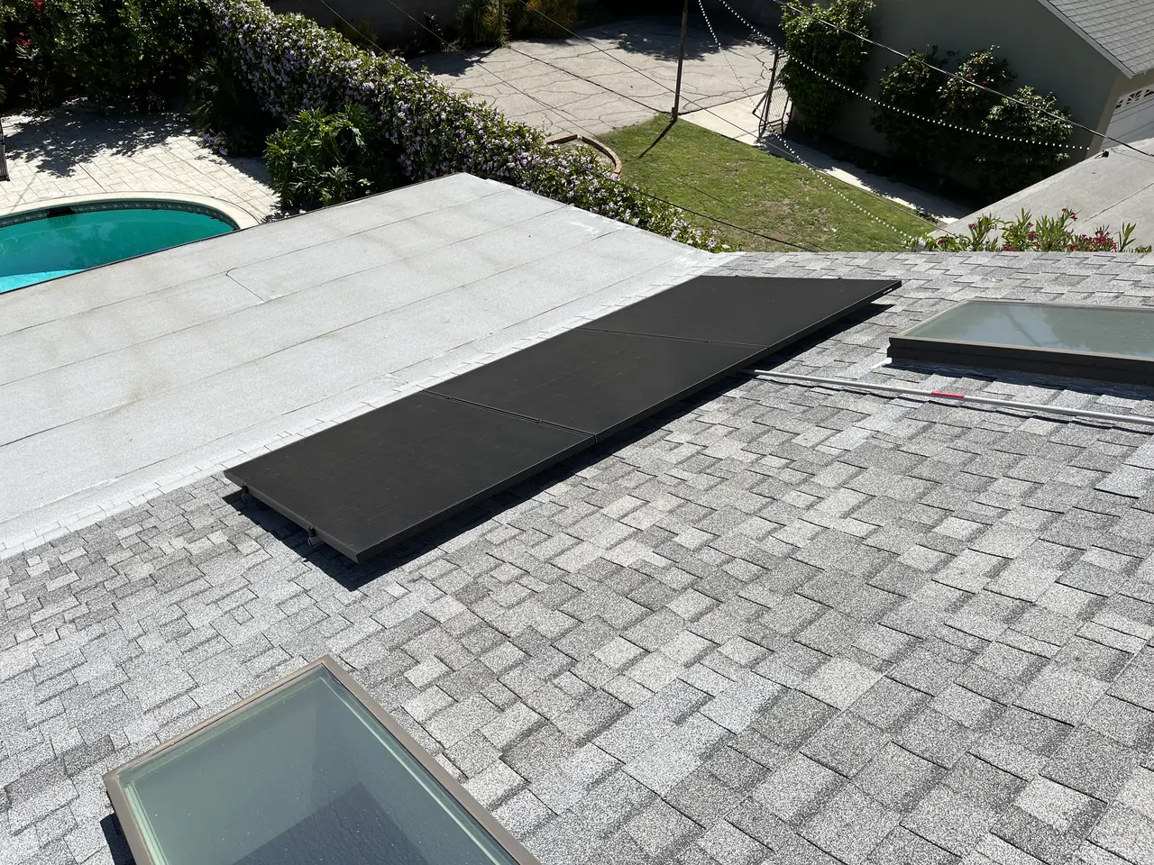 Black modules following the angled plane of a hip roof toward the ridge, with a swimming pool visible beyond, Van Nuys, Los Angeles