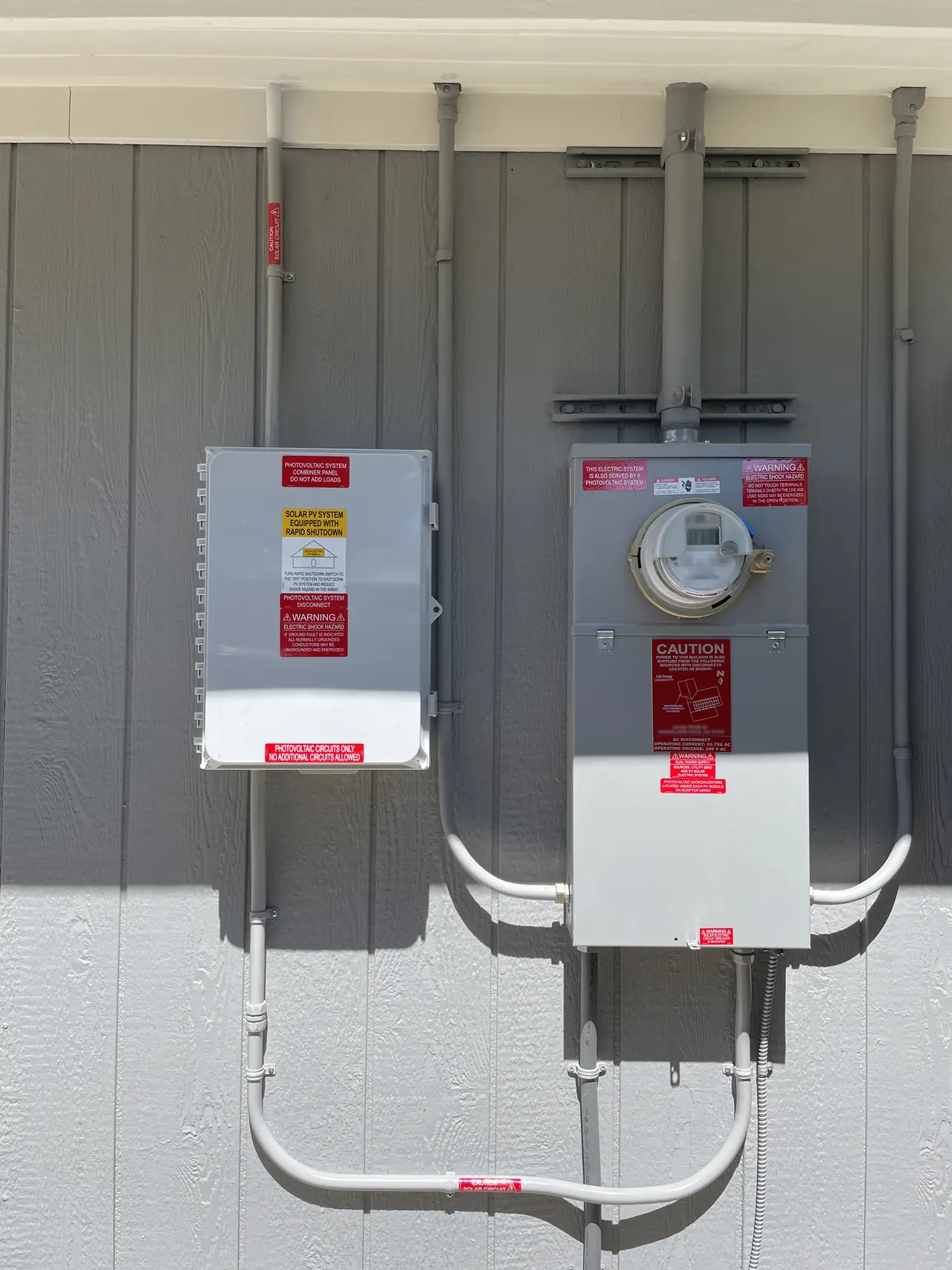 A closed solar disconnect and a meter panel side by side on a gray exterior wall with conduit running between them, Woodland Hills