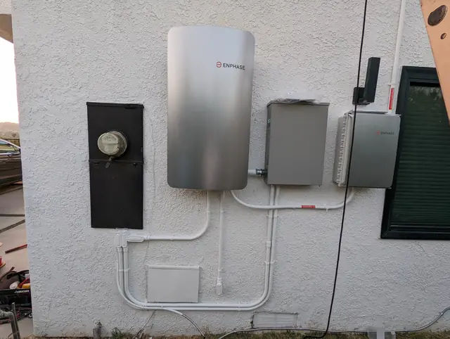 A battery, service panel, combiner and disconnects mounted in a row along a stucco exterior wall, Woodland Hills
