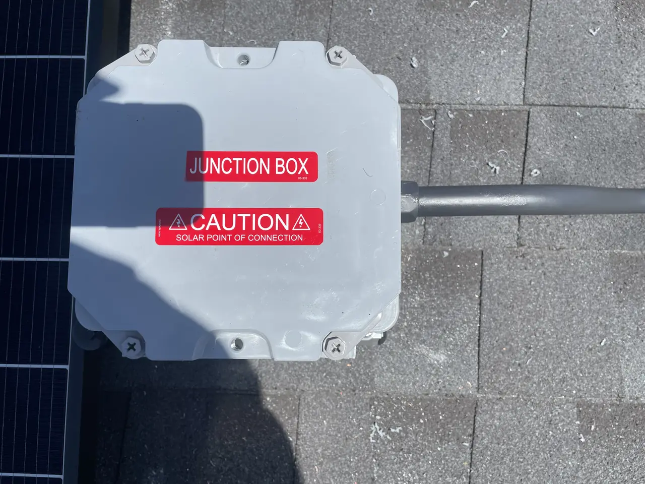 A closed junction box labeled as the solar point of connection, mounted on a shingle roof beside the edge of a module, Woodland Hills
