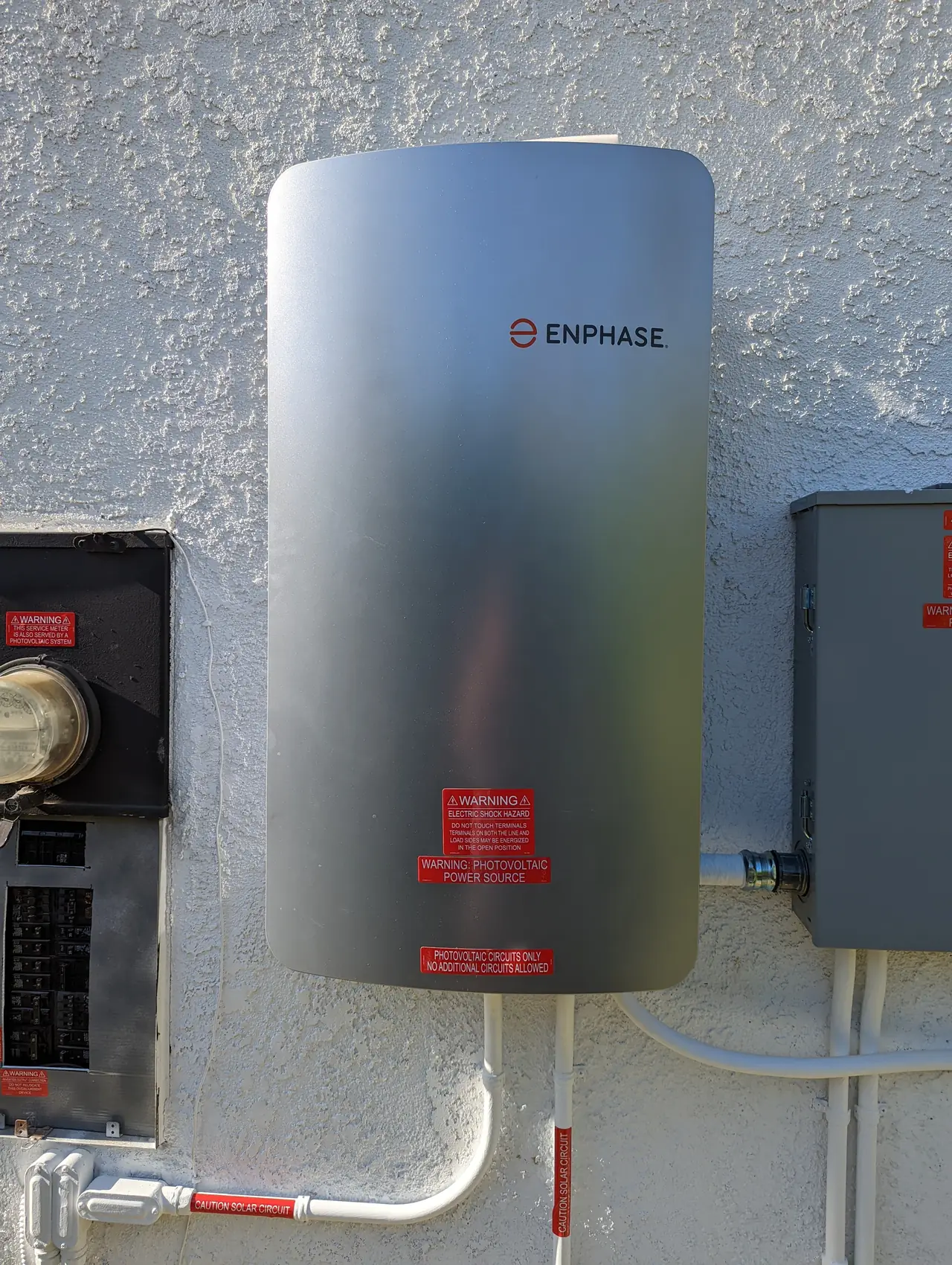 A tall Enphase battery enclosure mounted on a stucco wall beside the service panel with conduit running between them, Woodland Hills