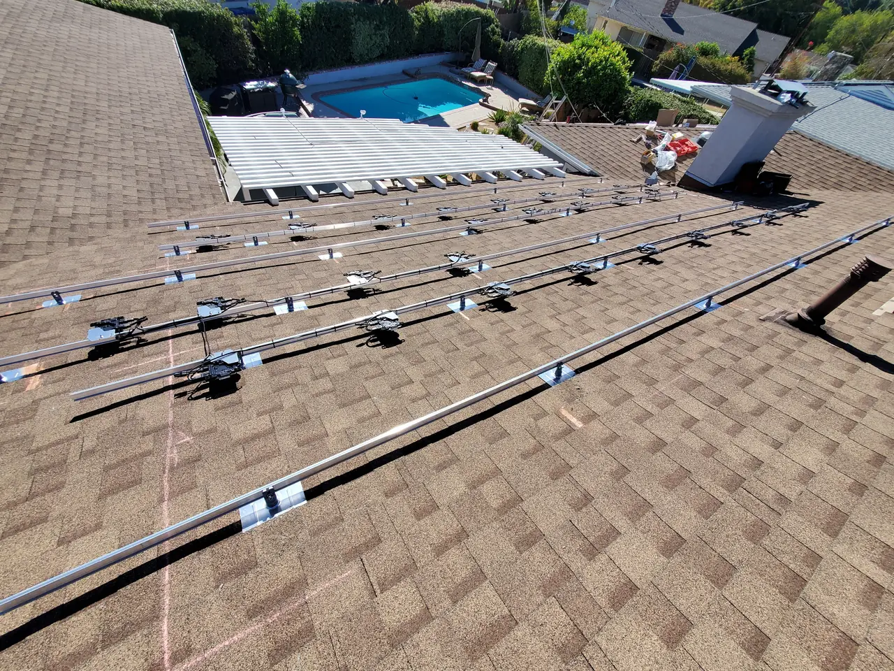 Mounting rails and microinverters laid out across a wide shingle roof before the modules are set, with a pool visible below, Woodland Hills