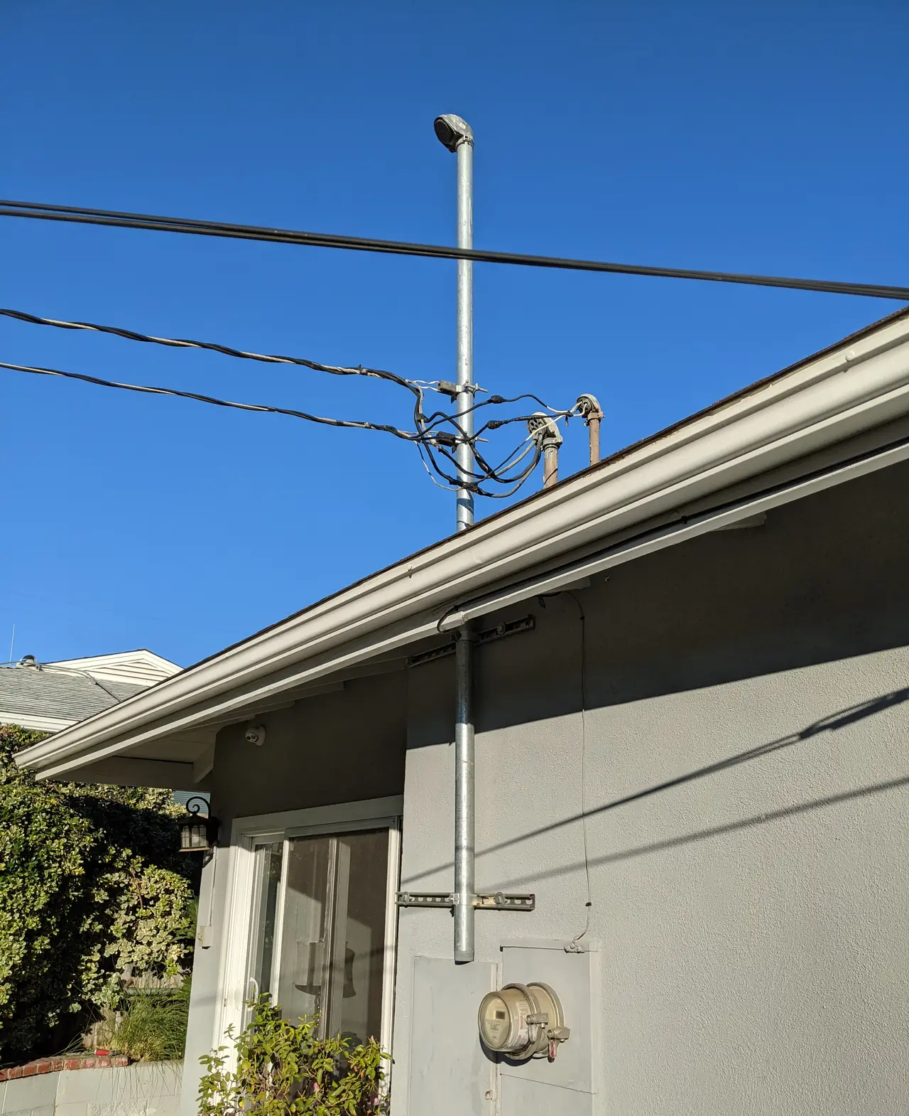 A service mast and meter on the stucco wall of a single-story house against a clear sky, Woodland Hills