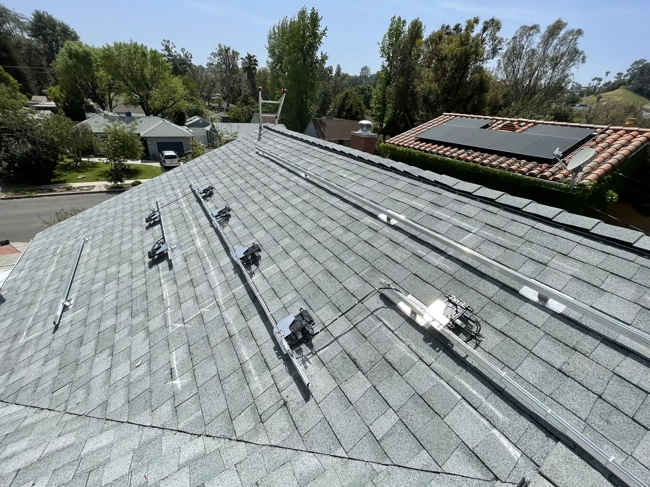Mounting rails and hardware set out across a new light gray shingle roof before the modules are installed, Woodland Hills