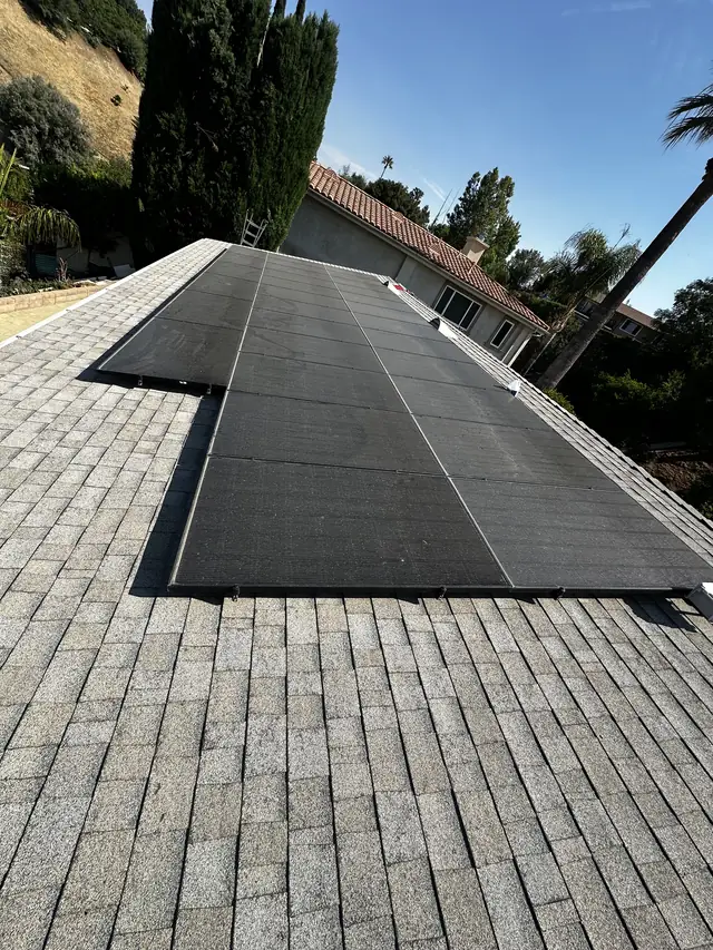 A black solar array along the ridge of a gray shingle roof with the neighborhood beyond, Woodland Hills