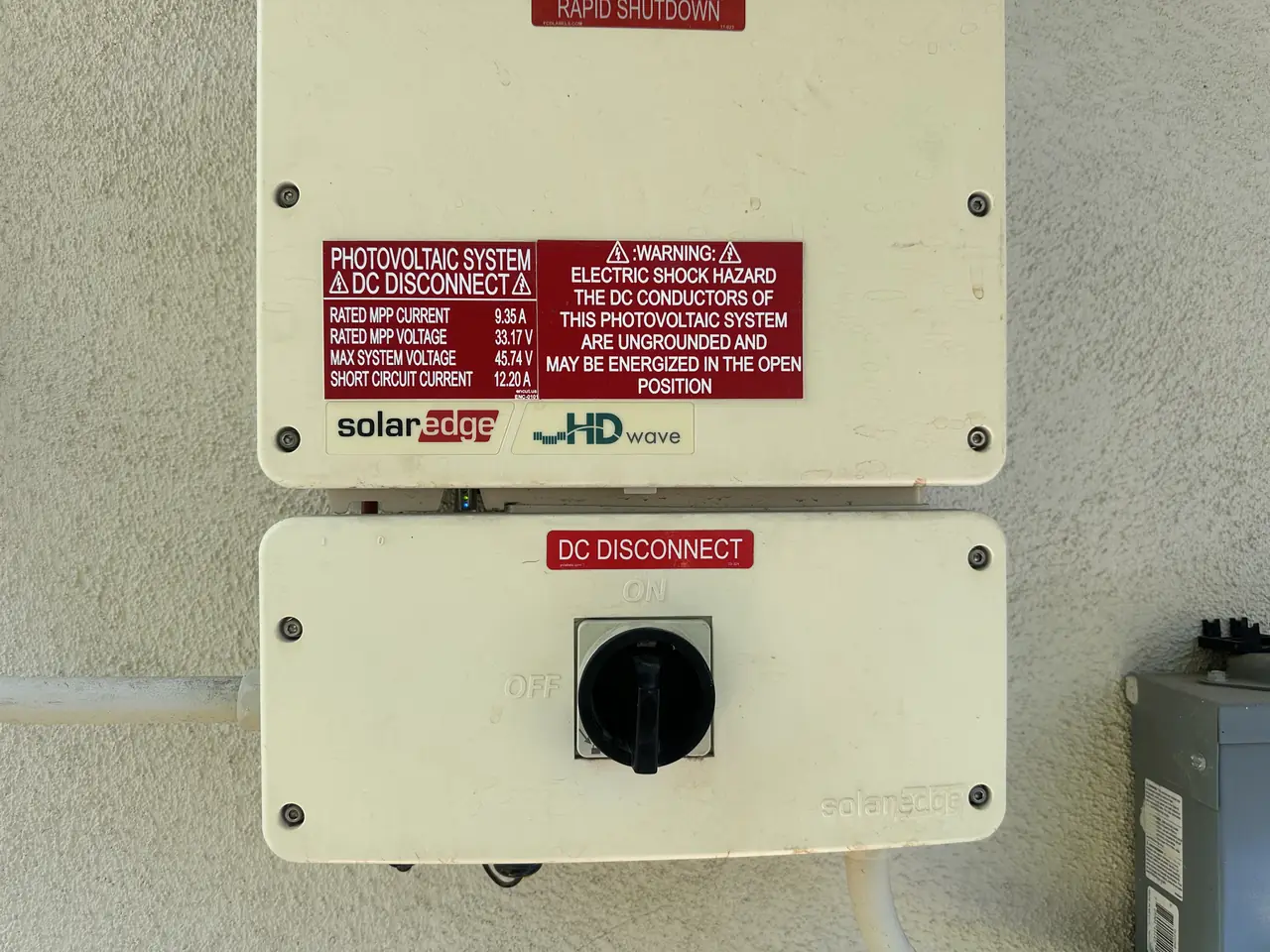 A wall-mounted SolarEdge string inverter with its direct-current disconnect below it on a stucco wall, Woodland Hills