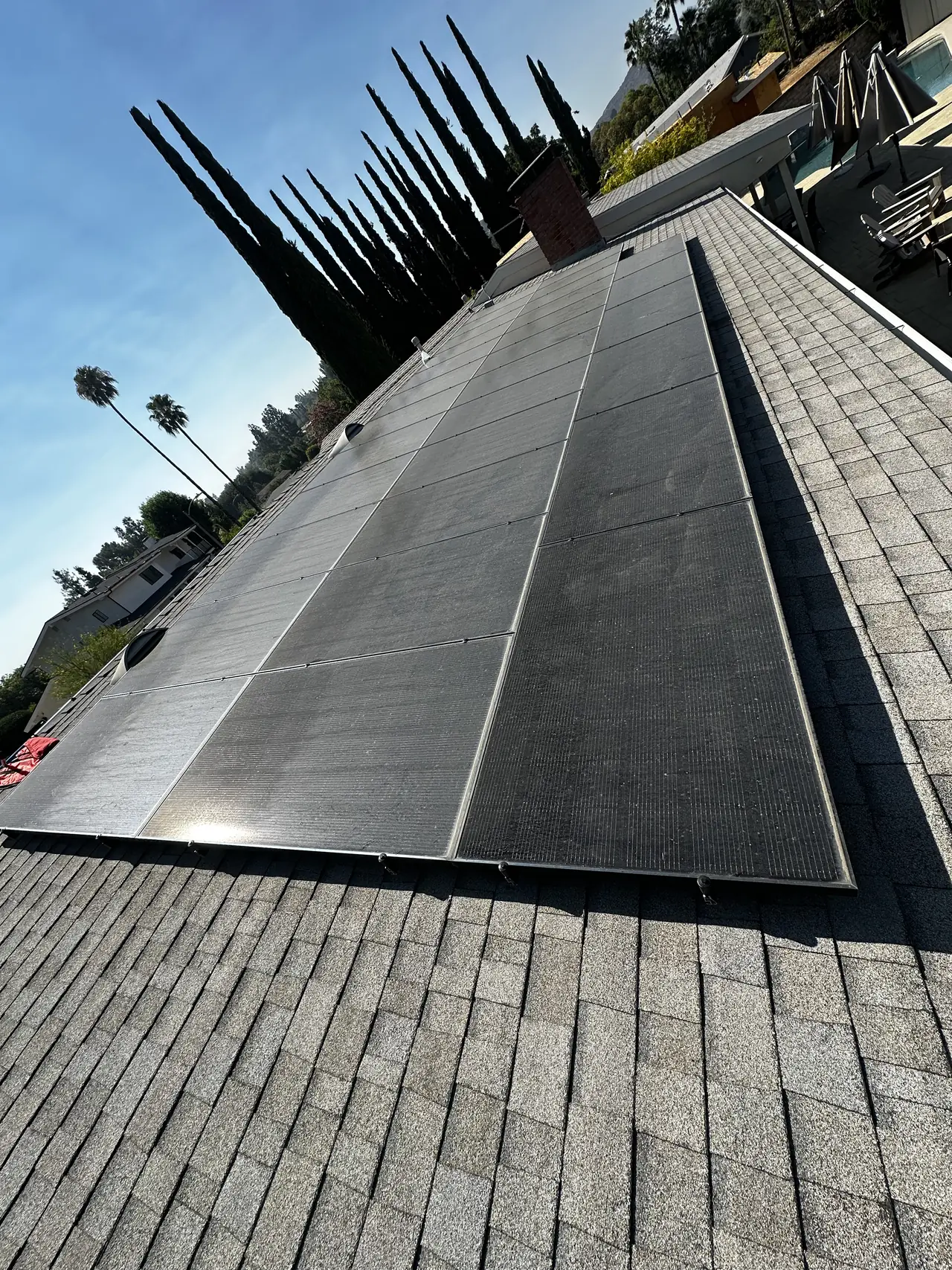 A black solar array on a gray shingle roof with the hillside and trees behind it, Woodland Hills