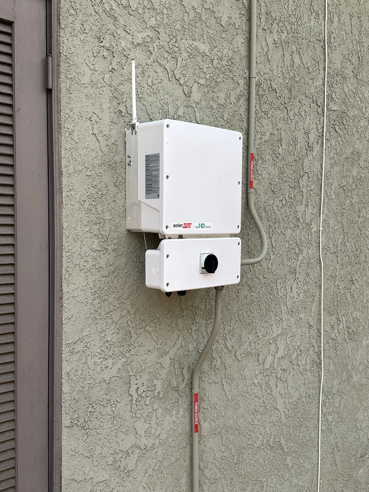 A replacement string inverter mounted on a stucco wall with conduit running down beside it, Woodland Hills