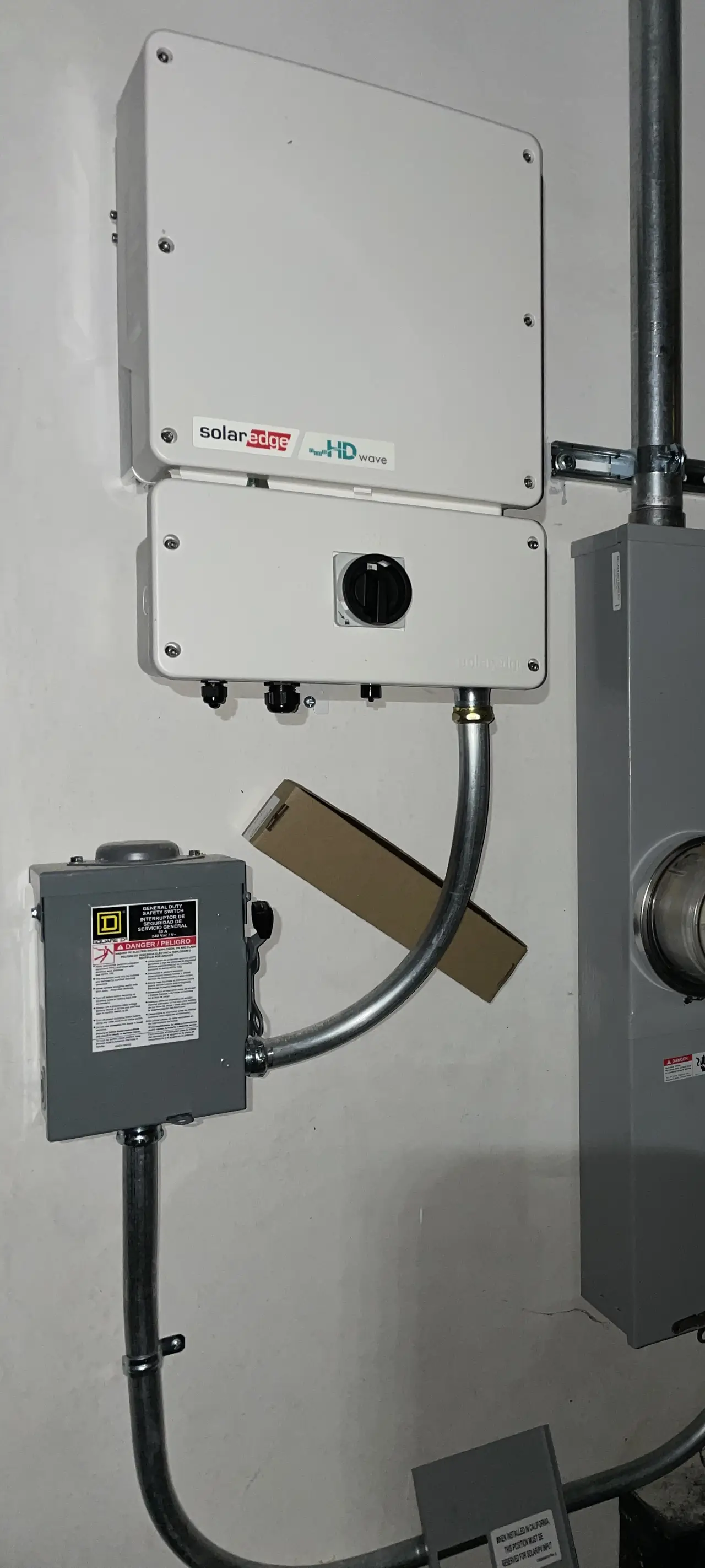 An inverter and a small disconnect mounted on a stucco wall, both closed and labeled, Woodland Hills